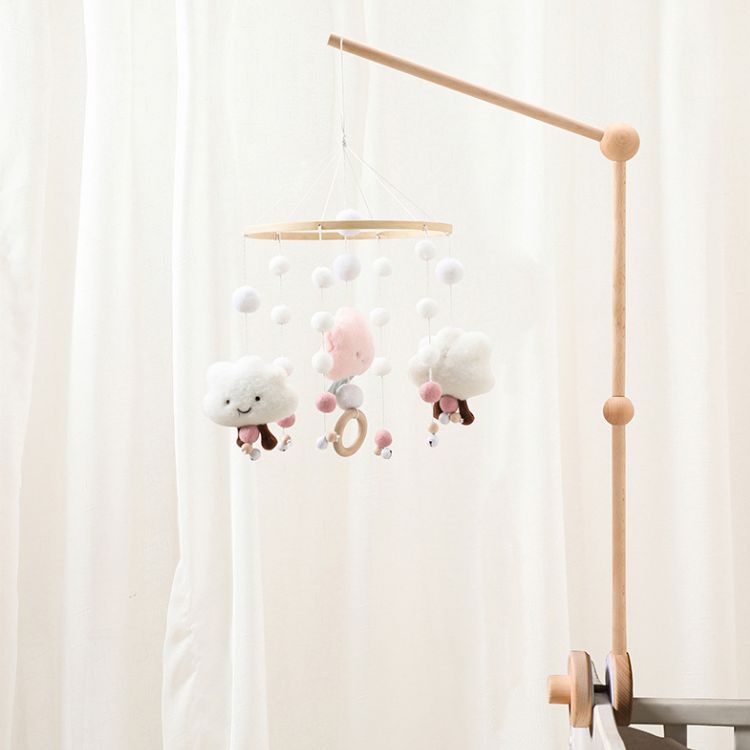 Children's mobile with clouds and animals hanging from a wooden stand against a white curtain.