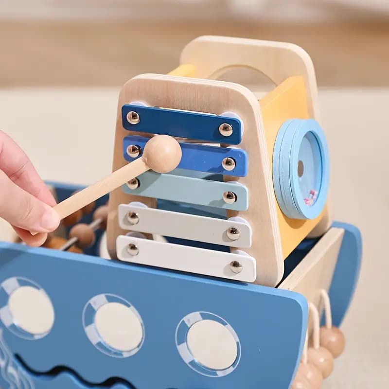 Wooden toy xylophone with blue and white bars and a wooden mallet, held by a hand.