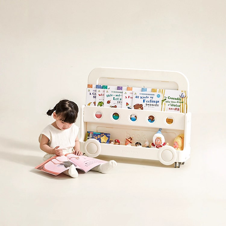 Child reading a book next to a children's playpen with toys and books on a white background