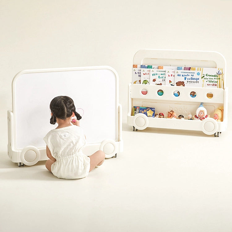 Child sitting in front of a whiteboard with a bookshelf filled with books and toys in the background.