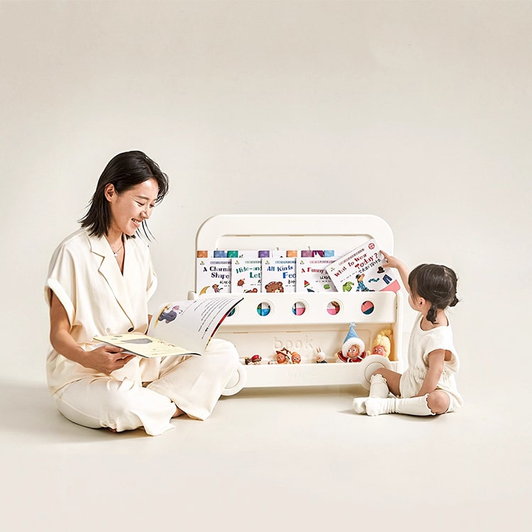 Woman and child sitting on the floor with a toy shelf and books in a minimalistic setting