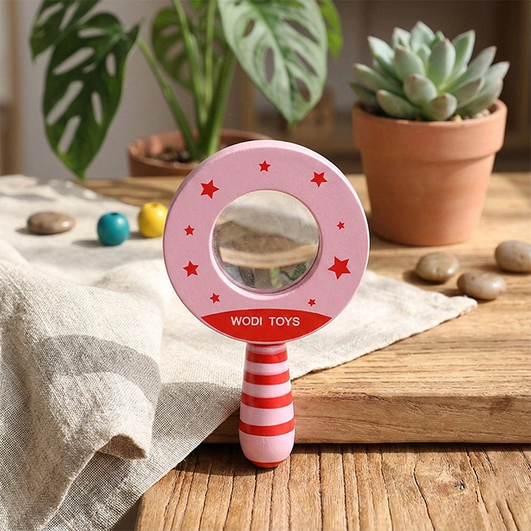 Magnifying Glass Toy | Pink toy mirror with red star patterns on a wooden surface with plants