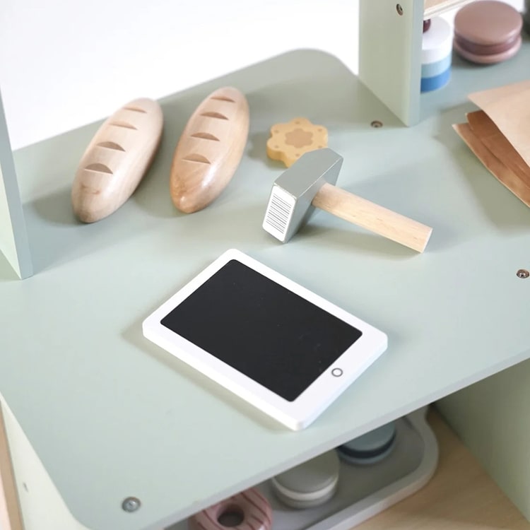 Children's play area with toys including a tablet, hammer, and wooden bread on a light green surface.